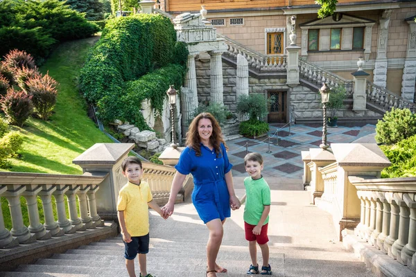 Genç bir kadın çocuklarıyla parkta oynarken eğleniyor. İlkokul çağındaki çocuklar. Aile pitoresk bitkilerle çevrili. Açık hava oyunları herkes için kullanışlı.