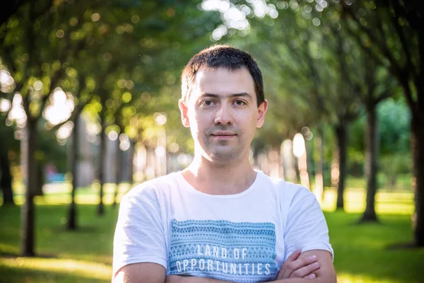 Açık havada beyaz gömlekli, doğa parkında gülümseyen güzel bir adamın portresini kapat. Moda modeli.