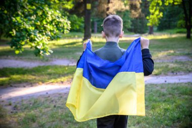 Ukrayna için dua et. Yaz parkını yöneten Ukrayna bayrağı taşıyan bir çocuk. Ulusal bayrak sallayan küçük çocuk barış için dua ediyor. Bağımsızlık Günü 'nü kutlayan mutlu çocuk.