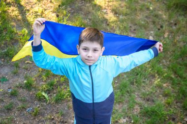 Ukrayna için dua et. Yaz parkını yöneten Ukrayna bayrağı taşıyan bir çocuk. Ulusal bayrak sallayan küçük çocuk barış için dua ediyor. Bağımsızlık Günü 'nü kutlayan mutlu çocuk.