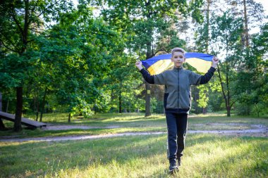 Ukrayna için dua et. Yaz parkını yöneten Ukrayna bayrağı taşıyan bir çocuk. Ulusal bayrak sallayan küçük çocuk barış için dua ediyor. Bağımsızlık Günü 'nü kutlayan mutlu çocuk.