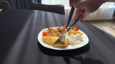 Çırpılmış yumurta salatası roka, kiraz domatesleri ve beyaz bir tabakta pesto soslu burrata. Bir kadın eli, yumuşak peyniri çatal ve bıçakla keser.. 