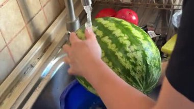 Akan suyun altında karpuz durulamak. Mutfak lavabosunda büyük meyveleri yıkıyorum. Musluk akışının altındaki büyük karpuzu temizliyorum. Yüksek kalite 4k görüntü