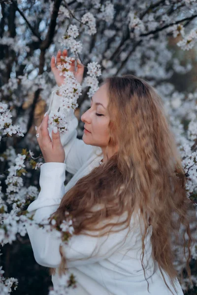 Fotoğrafta beyaz çiçeklerle açan bir ağacın yanında poz veren bir kız görüyorsunuz.