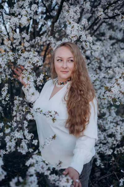 Fotoğrafta beyaz çiçeklerle açan ağacın yanında poz veren bir kızın portresini görüyorsunuz.