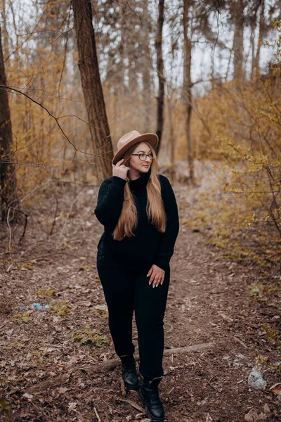 Resimde sonbahar ormanında yürüyen bir kız görebilirsiniz, sarı yapraklı ağaçların arasında yürüyen şapkalı bir kız..