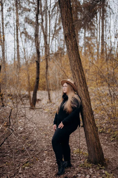 Resimde sonbahar ormanında yürüyen bir kız görebilirsiniz, sarı yapraklı ağaçların arasında yürüyen şapkalı bir kız..