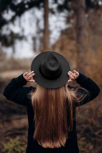 Resimde sonbahar ormanında yürüyen bir kız görebilirsiniz, sarı yapraklı ağaçların arasında yürüyen şapkalı bir kız..