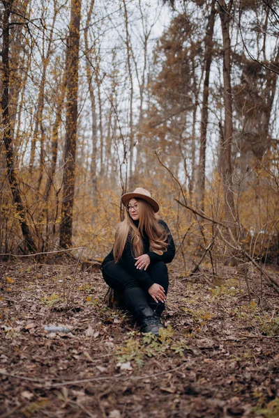 Resimde sonbahar ormanında yürüyen bir kız görebilirsiniz, sarı yapraklı ağaçların arasında yürüyen şapkalı bir kız..