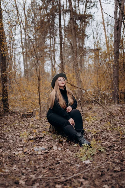 Resimde sonbahar ormanında yürüyen bir kız görebilirsiniz, sarı yapraklı ağaçların arasında yürüyen şapkalı bir kız..