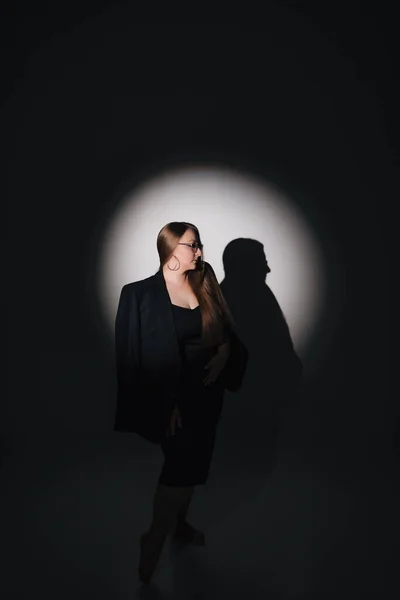 Siyah elbiseli, siyah ceketli, uzun sarı saçlı, siyah arkaplanda fotoğraf çeken bir kızın moda fotoğrafı.