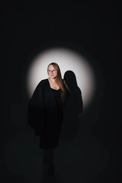 Siyah elbiseli, siyah ceketli, uzun sarı saçlı, siyah arkaplanda fotoğraf çeken bir kızın moda fotoğrafı.