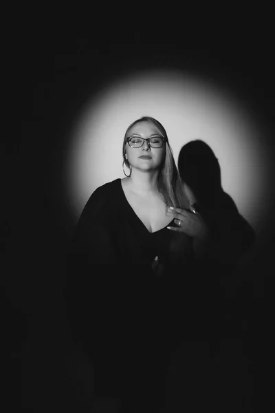 Siyah elbiseli, siyah ceketli, uzun sarı saçlı, siyah arkaplanda fotoğraf çeken bir kızın moda fotoğrafı.