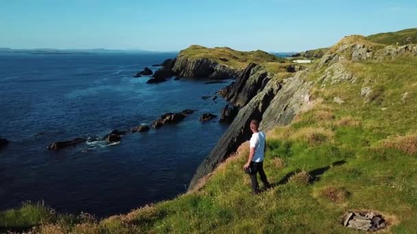A man on the edge of the cliff of Island holds a drone console in his hand and smile — Stock Video