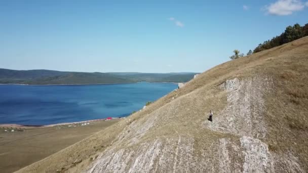 A man in a white shirt and waistcoat playing bass guitar on a mountain. Aerial view — Stock Video
