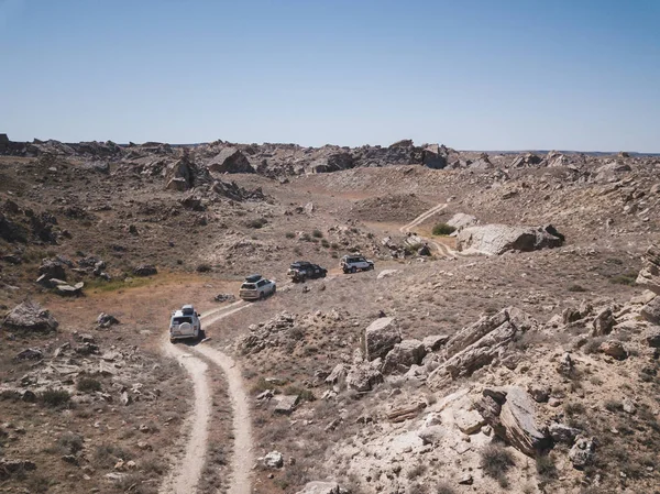 Ein Autokonvoi durchquert die Steppe zwischen Staub und Steinen. Luftaufnahme in Kazahstan lizenzfreie Stockfotos