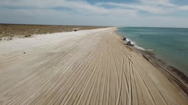Los coches conducen a lo largo de la playa de arena creando aerosoles de agua. Vista aérea — Vídeos de Stock
