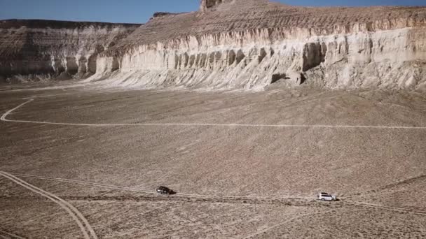 Paisagem épica. Dois carros atravessam o deserto entre as montanhas. Vista aérea — Vídeo de Stock