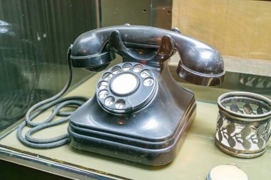 Cam bir vitrin içinde eski moda siyah döner telefon, muhtemelen bir müze ortamında belirgin bir şekilde dekoratif metal işçiliği veya heykeltraş Siyah ve beyaz renk şeması Pro ile sergileniyor.