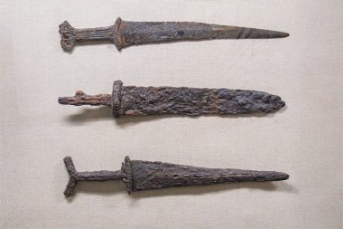 Kıvrımlı bir yüzey üzerinde doğrusal düzende üç paslı, eski kılıç, kırmızımsı-kahverengi korozyon ve yumuşak gölgeler ile çevresel ışıklandırma gerçekçilik stili dokusu ve detaya odaklı açılı persp