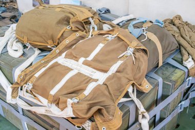 Askeri teçhizatlı açık hava sahnesi metal bir yapıya bağlanmış iki zeytin yeşili çanta, muhtemelen araç ya da ekipman uçak gövdesi kalıntılarında ipucu yok.