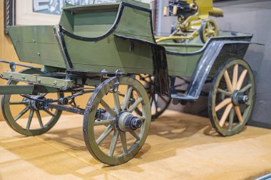 Klasik zeytin yeşili, motorlu keşif aracı müze ortamında at yok, dört tekerlekli, parlak ışıklandırma ve kenar açılı perspektif.