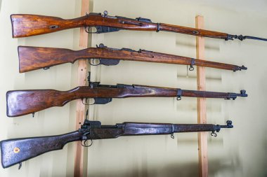 Altı antika tüfek koleksiyonu ahşap bir rafa düzgünce yerleştirilmiş, iki sıra halinde yatay olarak monte edilmiş, görünürde hiçbir metin veya ek içerik yok, kapalı alanda bile yumuşak döküm ışık