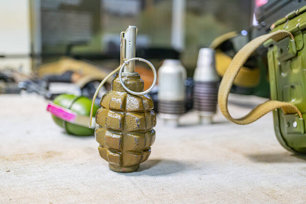 На изображении изображена военная сцена с двумя зелеными взрывчатыми веществами на деревянном столе, а также шлем и несколько круглых контейнеров.