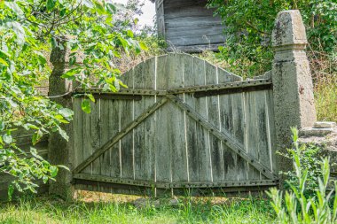 Antik Orta Avrupa köyü yıpranmış, geleneksel tasarımı ve çeşitli tonları olan kırsal ahşap kapı. Arka planda yaprak döken ağaçlar, yumuşak ışıklandırma.