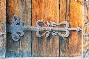 Eski bir Orta Avrupa köyünün yıpranmış ahşap kapısının yaşlanmış, süslü metal bir mandalının yakın çekimi.