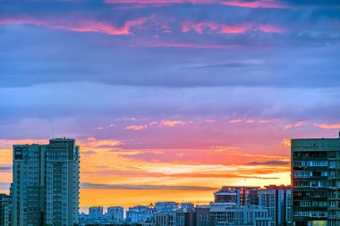 Gün batımında canlı bir şehir manzarası olan Kyiv 'de, rengarenk gökyüzüne karşı muhtelif boyutlarda siluetleri olan binalar var.