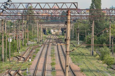 Çim ve çalı, bulutlu gökyüzü, binalar veya depolama tesisleri, elektrik hatları olan sanayi kentlerinde demiryolu ayrımı yapılıyor.