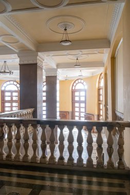 Karmaşık tasarımları, uzun kemerli pencereleri, parlak zeminleri, sütunları, avizeleri ve süslü bir balkonu olan eski Avrupa salonu. Sıcak renk paleti, doğal ışık filtresi.