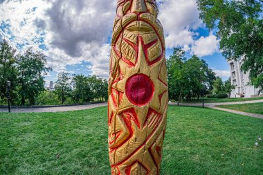 Parkta alev şeklinde sarı, kırmızı ve turuncu heykel ya da bahçeli ağaçlar ve mavi gökyüzü öğleden sonra ya da akşam üzeri aydınlatma şeklinde.