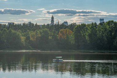 Motorlu tekne, jet ski, şehir silueti, yeşil ağaçlar, parçalı bulutlu gökyüzü, doğal ışık, gerçekçi tarz, genel bakış açısı, metin yok.