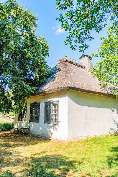 Сельский центральноевропейский одноэтажный соломенный коттедж, осенняя обстановка с деревьями, окнами, ставнями, дымоходом, днем, натуралистическими красками