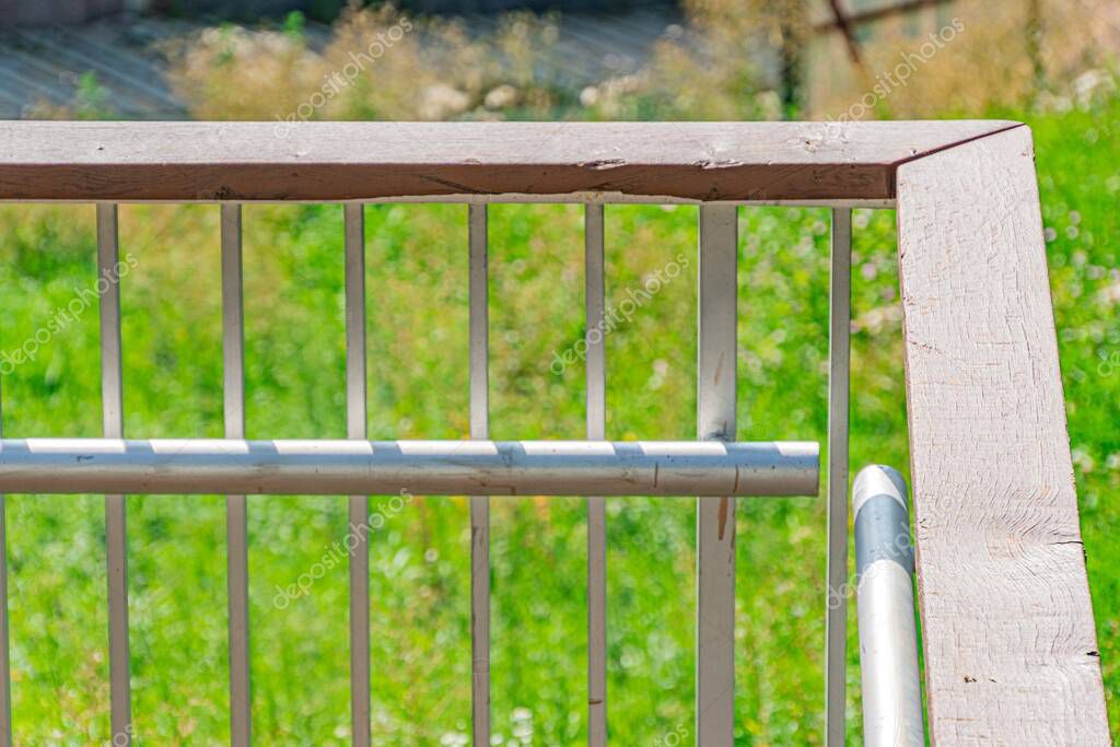 Close-up of a grey metal railing with green background, utilitarian, outdoor setting possibly park or garden, no distinct shadows, no texts or logos