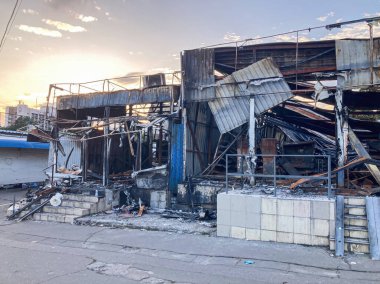 Yanmış şehir binası, tahrip olmuş iç mekan, enkaz, paslanmış metal kirişler, çatlak kaldırımlar, kırık fayanslar, atılmış çöpler, beton, zemin kat perspektif, yumuşak ışık, uzun gölgeler, klostrofobi