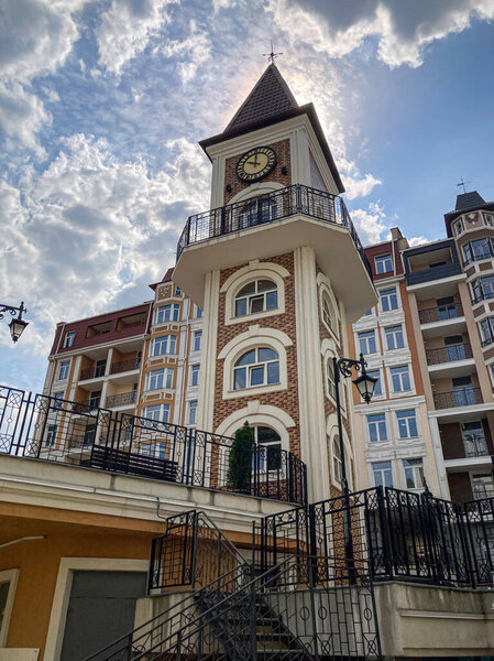 Ornate brick building with clock tower, overcast skies, small plaza, greenery, reddish-brown facade, arched windows, decorative columns, pointed roof, natural lighting, angled viewpoint