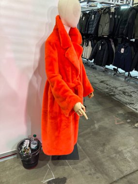 Giysi rafları arasında turuncu sahte kürk manklü manken, çeşitli giysi arkaplanı yakınlardaki siyah çöp tenekesi yere saçılmış şişeler Kyiv, Ukrayna 07-31-2025