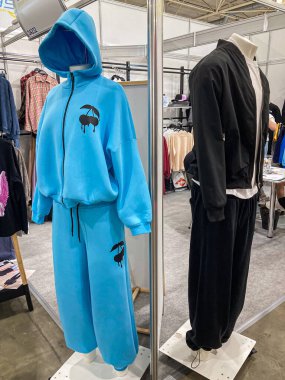 Mavi ve siyah spor kıyafetleri, iyi ışıklandırılmış bir sergi salonunda sergileniyor. Beton döşeme, Ba Kyiv, Ukrayna 07-31-2025 'te ilave giysi içeren askılar.