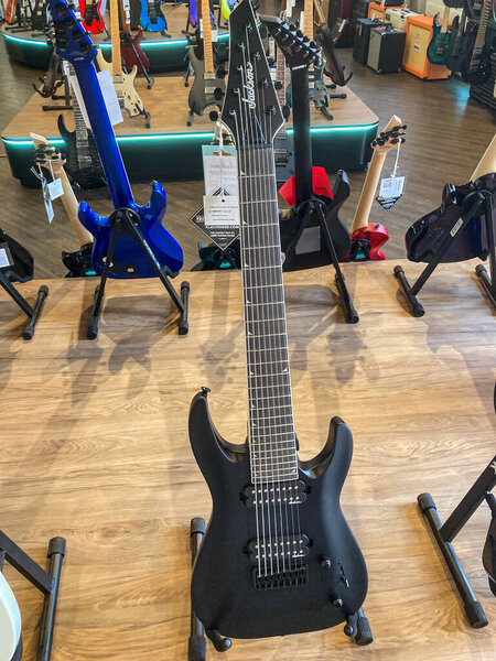 Two electric guitars, one black and blue, the other red, on display in a well-lit music store The foreground guitar is futuristic with contrasting wooden stand Bac Kyiv, Ukraine 08-06-2025