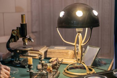 Antika eczane dolabı, mikroskoplar, bilimsel ekipmanlar, test tüpleri, yeşil-gri bez, antika masa lambası, antika laboratuvar ayarları.