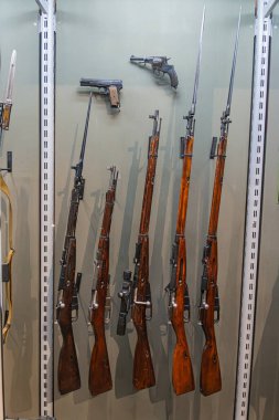 Tüfeklerin cam bir kutuda sergilenmesi, metal raflar, dikey olarak dizilmiş ve ahşap stokların üzerinden aydınlatılmış, esasen kahverengi veya siyah, ve çeşitli varil uzunlukları ile