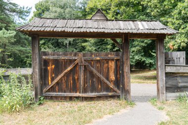 Park benzeri köy ortamında antik ahşap Ortodoks kilisesi, yıpranmış dış görünüşü ve iç kısımlarını gösteriyor. Sönük toprak renkleri, doğal ışıklandırma, sakin atmosfer.
