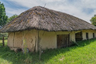 Eski Avrupa kır evi sazdan çatılı, muhtemelen toprak yapım koçanı ya da benzeri, birden fazla pencere, aşınmış ve yaşlanmış dış görünüş, yeşil alan ayarı, parlak gün ışığı, dağınık bulutlar, Peo yok