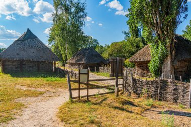 Eski, Orta Avrupa kırsal köyünde sazdan kulübeler ve tahta bir kapı, açık gökyüzünün altında, kuru, tozlu bir yol üzerinde