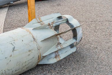 Geniş gri askeri mermi, sivri burunlu silindirik şekilli, arka planda bariyer yapısı olan asfaltlı bir yolda uzanan paslı doğal ışıklandırma, hafif yükseklik, bulutlu.
