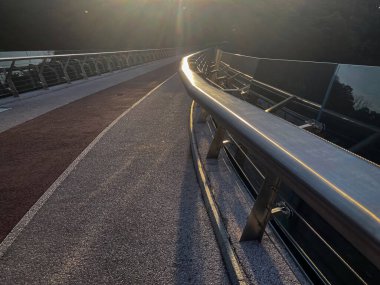 Yuvarlak ışıklı, modern metal korkuluklu ve dokulu yüzeyi olan bir yaya köprüsünün gündüz görüntüsü görünürde kimse olmadan, bir Nat 'a karşı mimari bir çekim yaparken görüntüsü sakin.