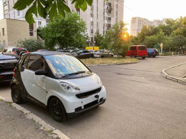 Şehir caddesinde gün batımında sabit duran üç tekerlekli, tek renkli konsept araba diğer park halindeki arabalar, konut binaları ve yayalar ile birlikte Los Angeles 'la birlikte yenilikçi tasarım.